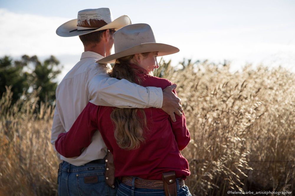 A couple in western attire embracing against a backdrop of golden prairie grass.