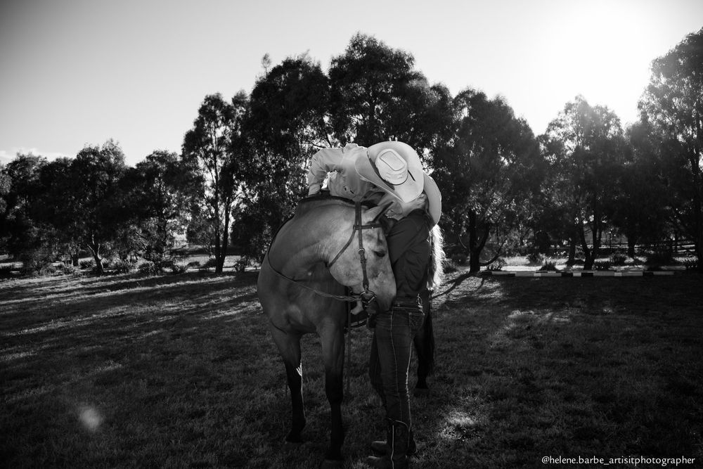 A black and white photo of a horse and rider silhouetted against trees in natural lighting.
