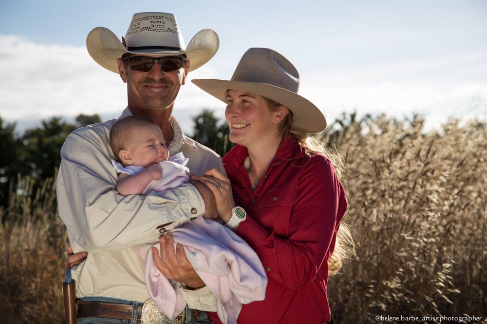 A family in cowboy hats shares a tender moment with their baby in a sunny field.