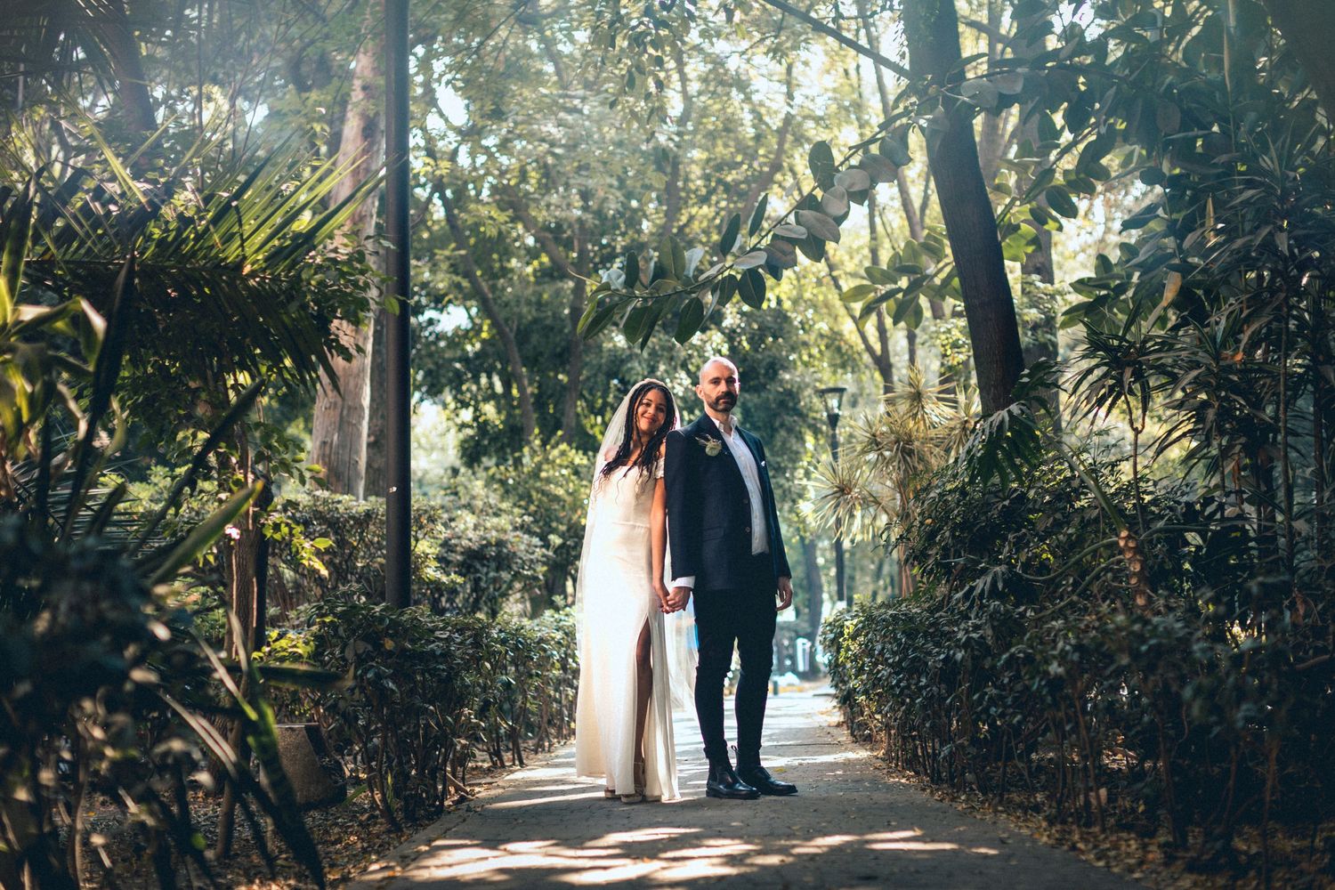 Wedding couple walking together on outdoor garden path surrounded by greenery.