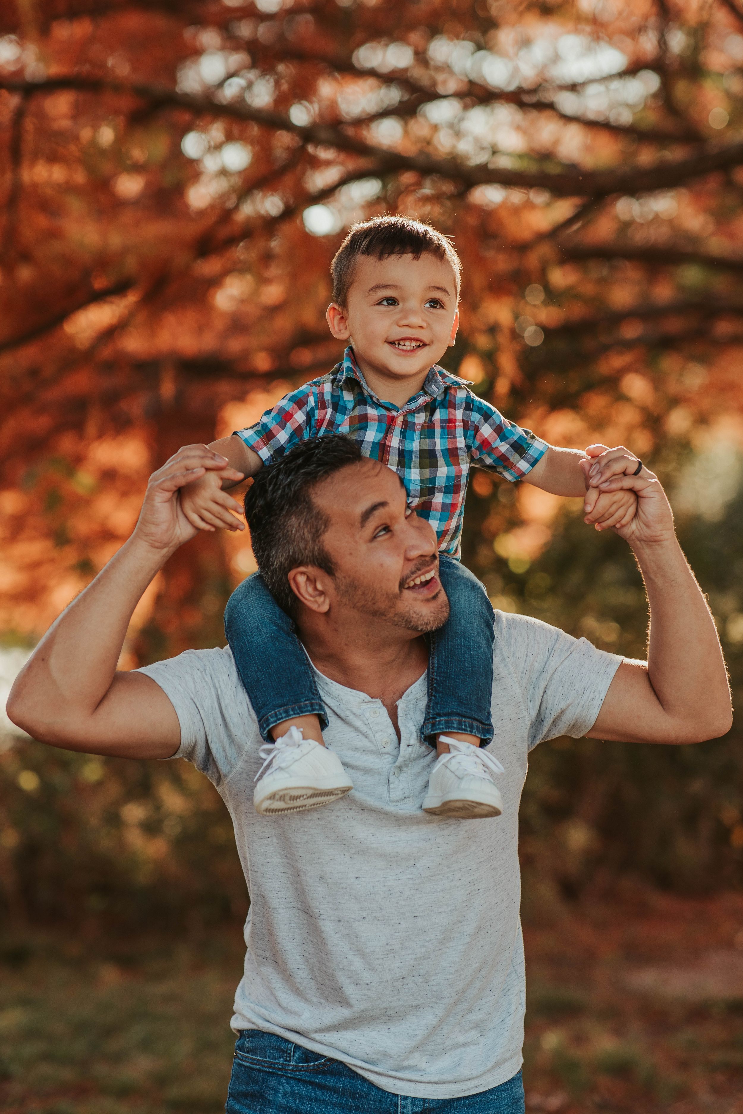 Playful autumn family moment with shoulders rides against vibrant fall foliage.
