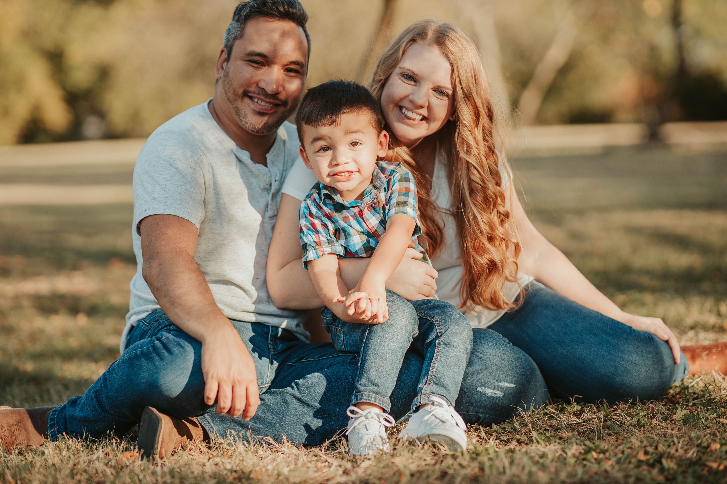 Relaxed outdoor family photo session on grass with warm sunset lighting.