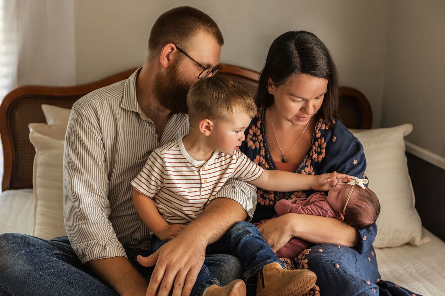 Family relaxing together on bed while looking at newborn baby.