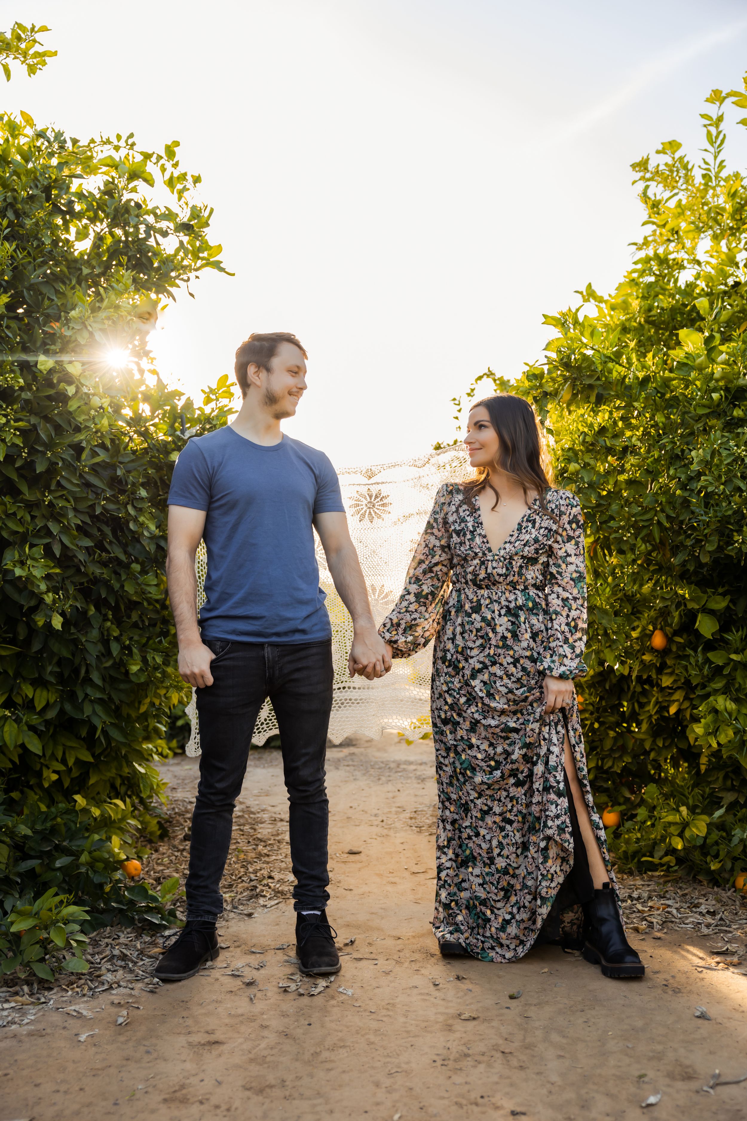 A couple holds hands while walking through a citrus grove at golden hour.