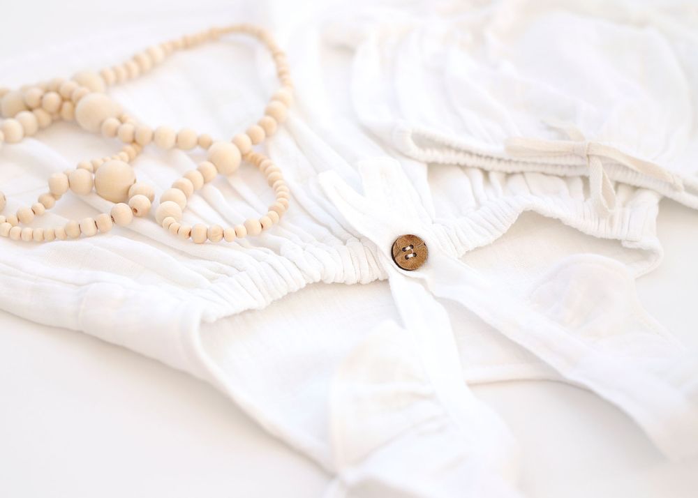 White fabric with wooden button detail and pearl necklace.