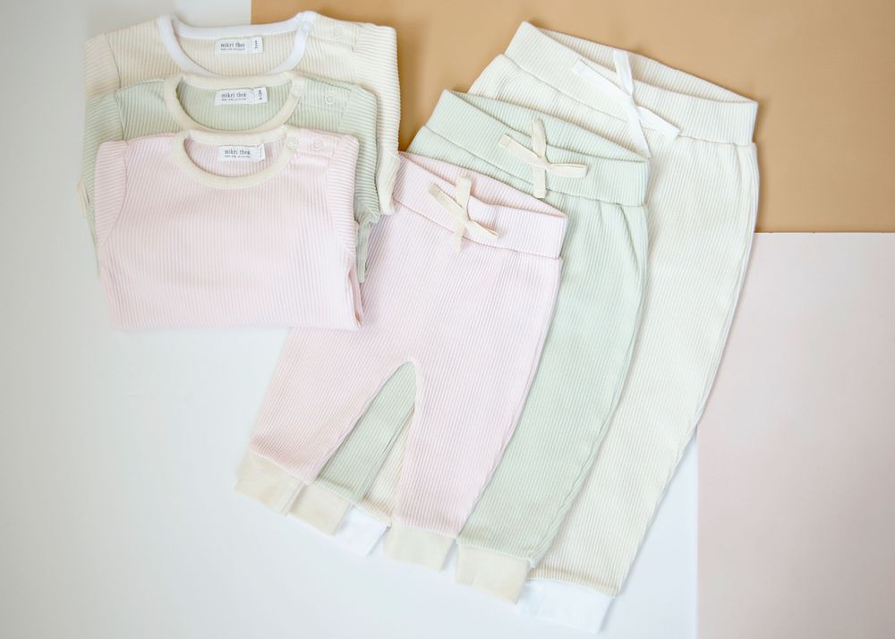 Soft pastel colored baby clothing neatly folded on beige background.