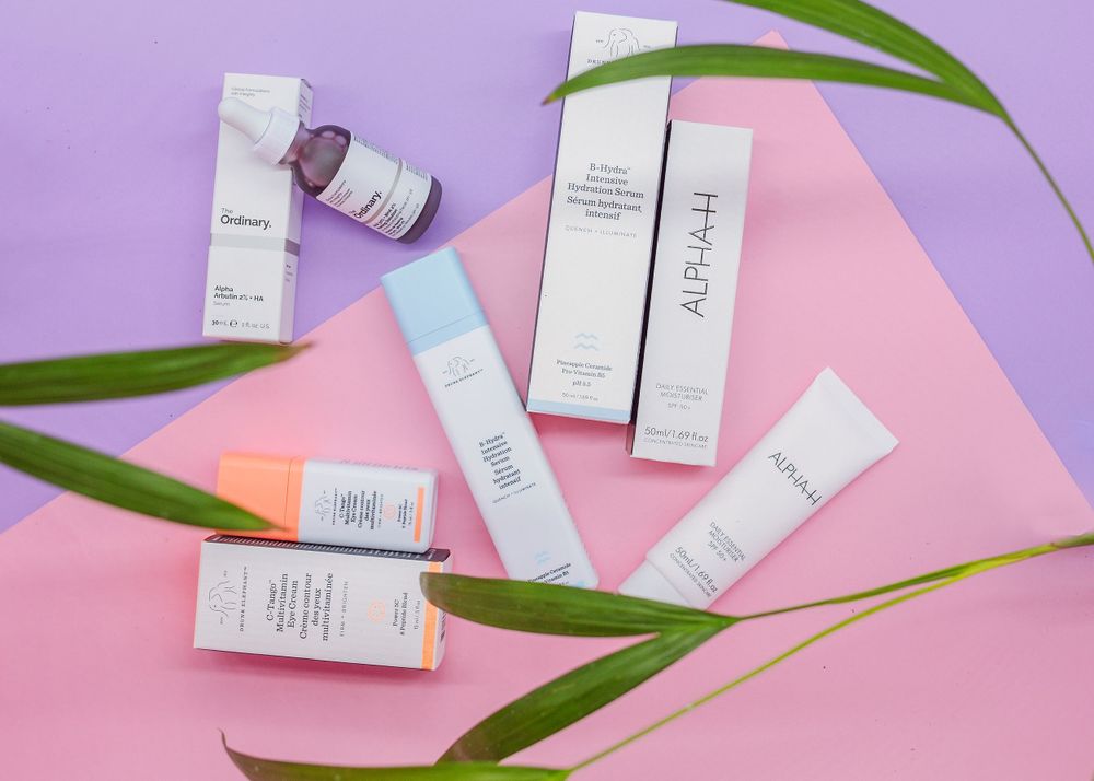 Skincare products and green palm leaves arranged on pink and purple background for beauty flatlay.