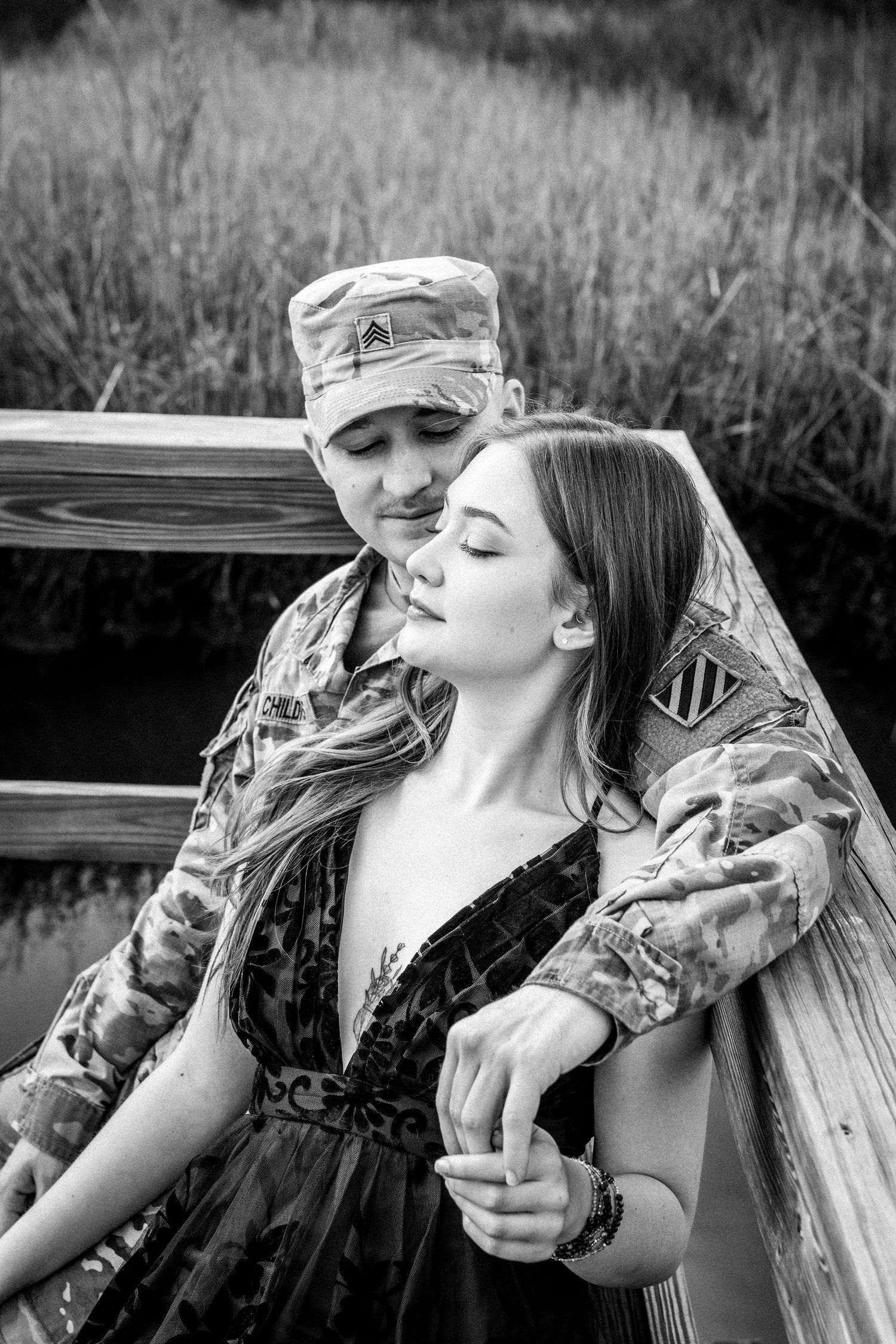 An intimate black and white portrait of a couple sharing a tender moment on a wooden deck.