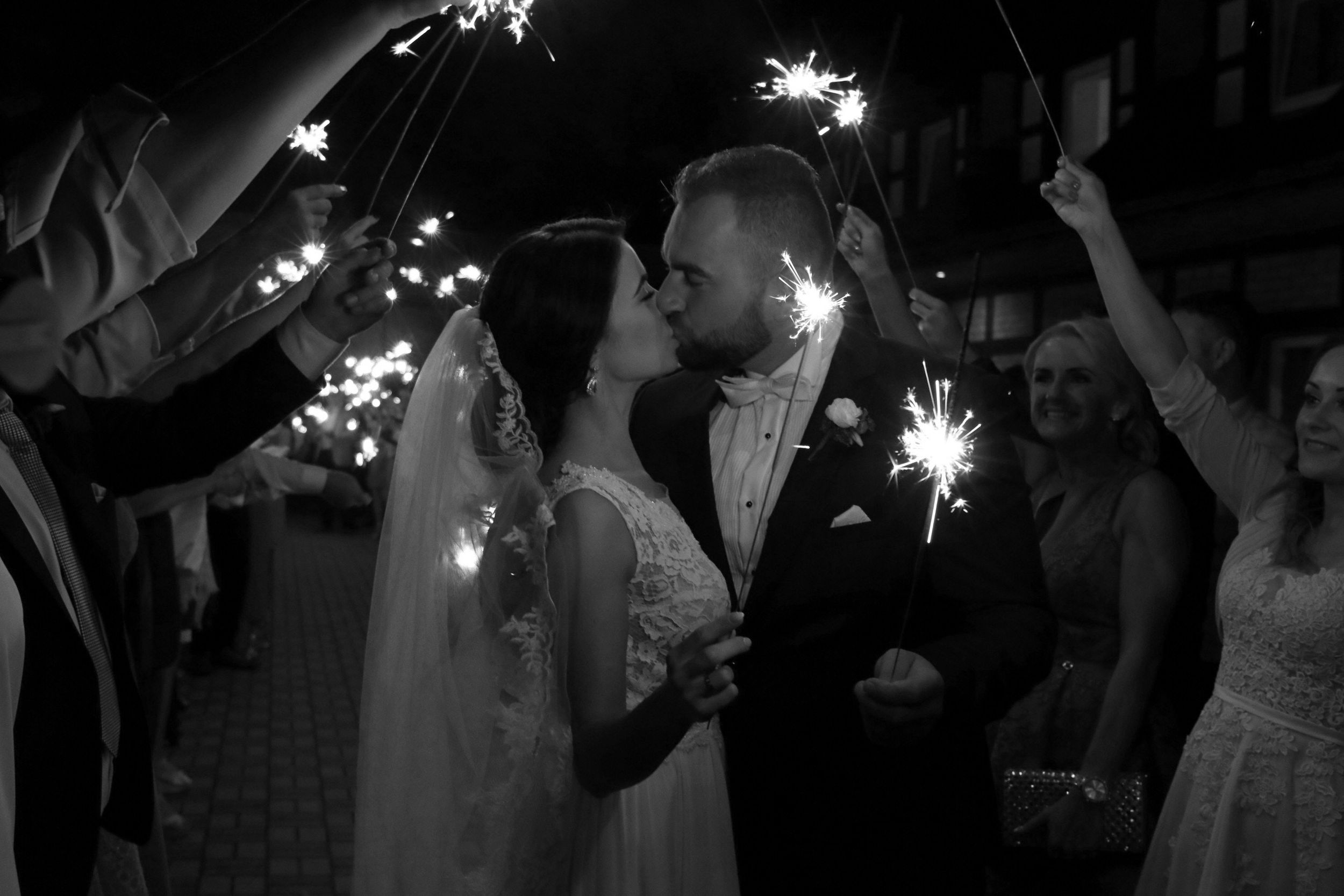 Bride and Groom kissing each other while guests are holding sparklers at night
