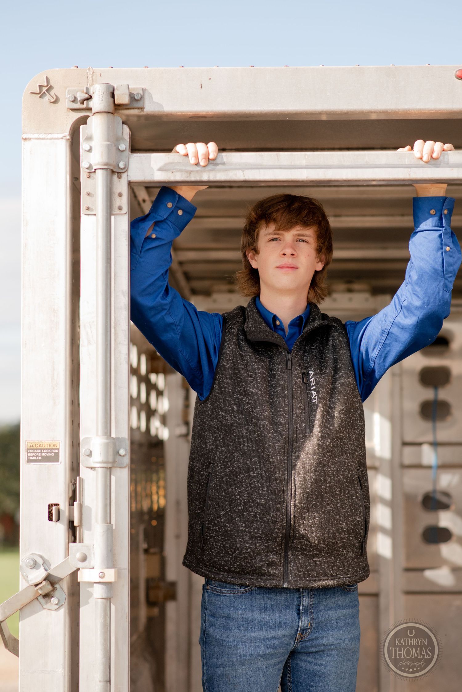 Figure in blue jacket and dark vest poses inside metal livestock transport trailer.