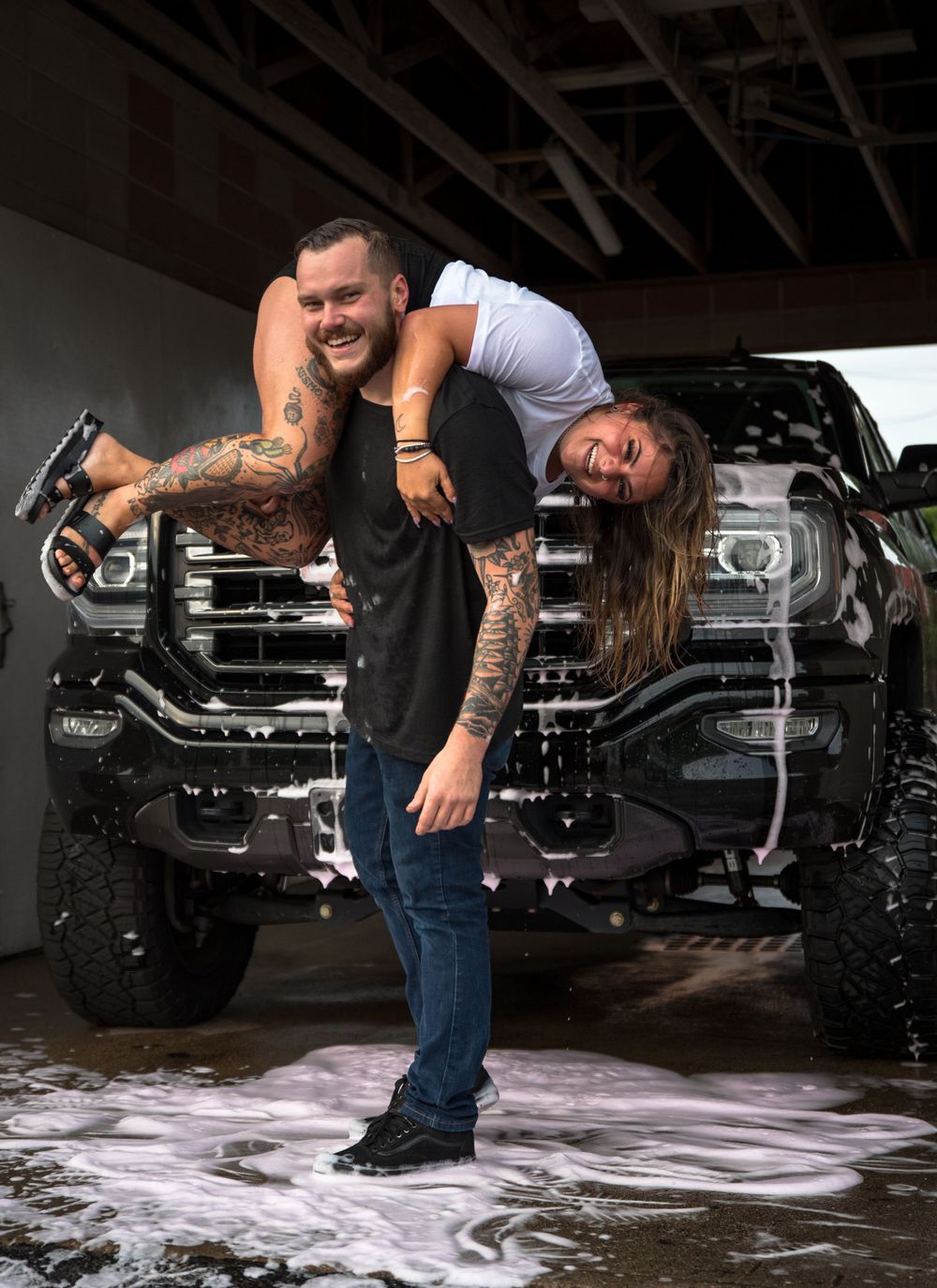 Playful couple interacting near trucks with water splashing.