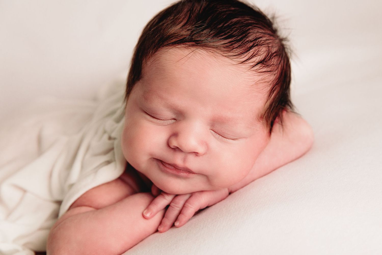 close up of baby boy laying on stomach, chin resting on the back of his hands smiling