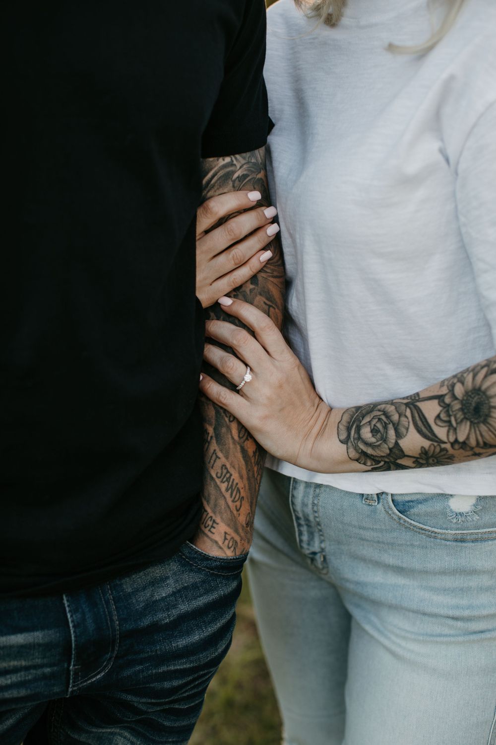 Close-up of tattooed couple holding arms together, woman showing engagement ring on her hand.