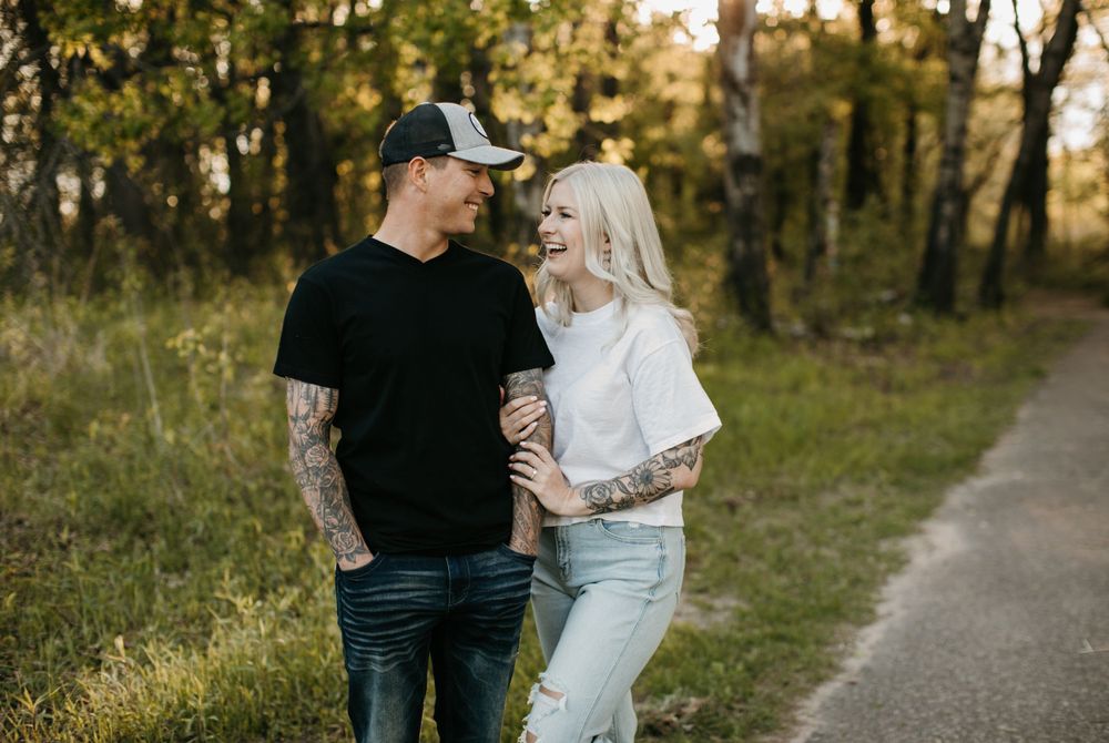 Smiling tattooed couple walking together on a forest path during golden hour sunset.
