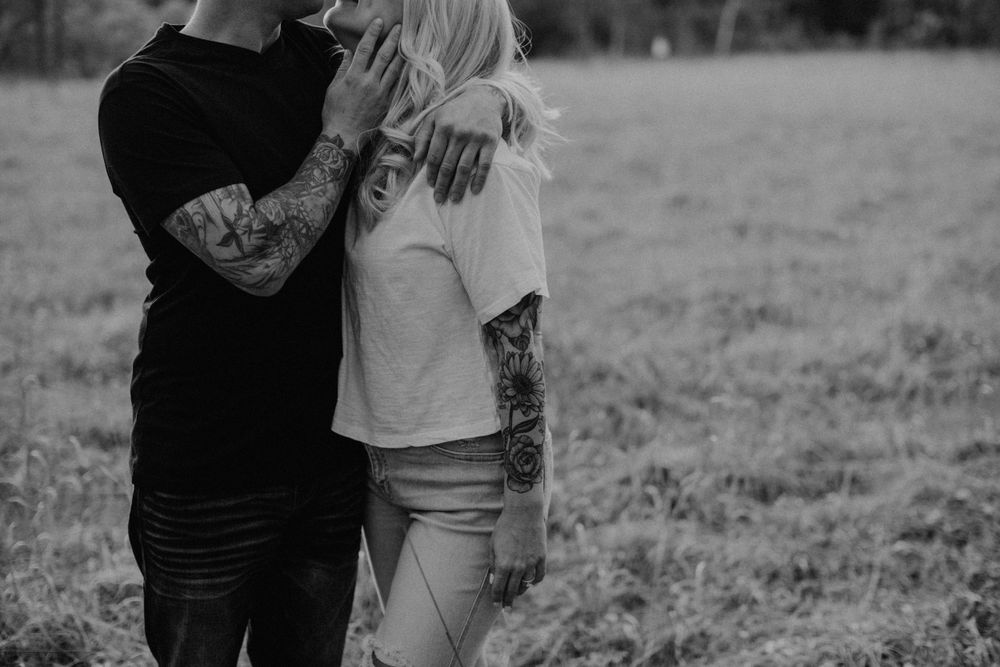 Tattooed couple embracing in a grassy field, black and white romantic outdoor photo.