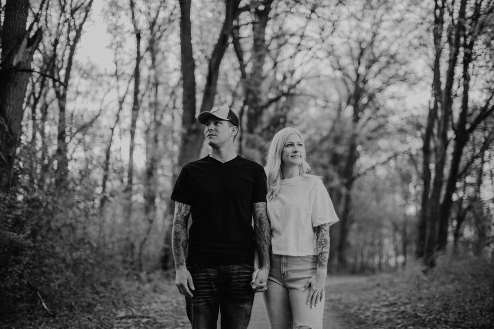 Tattooed couple holding hands on a woodland path, moody black and white forest portrait.