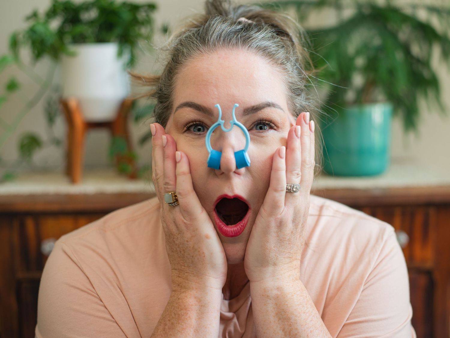 Woman with surprised expression and blue nose paint holds hands to face.