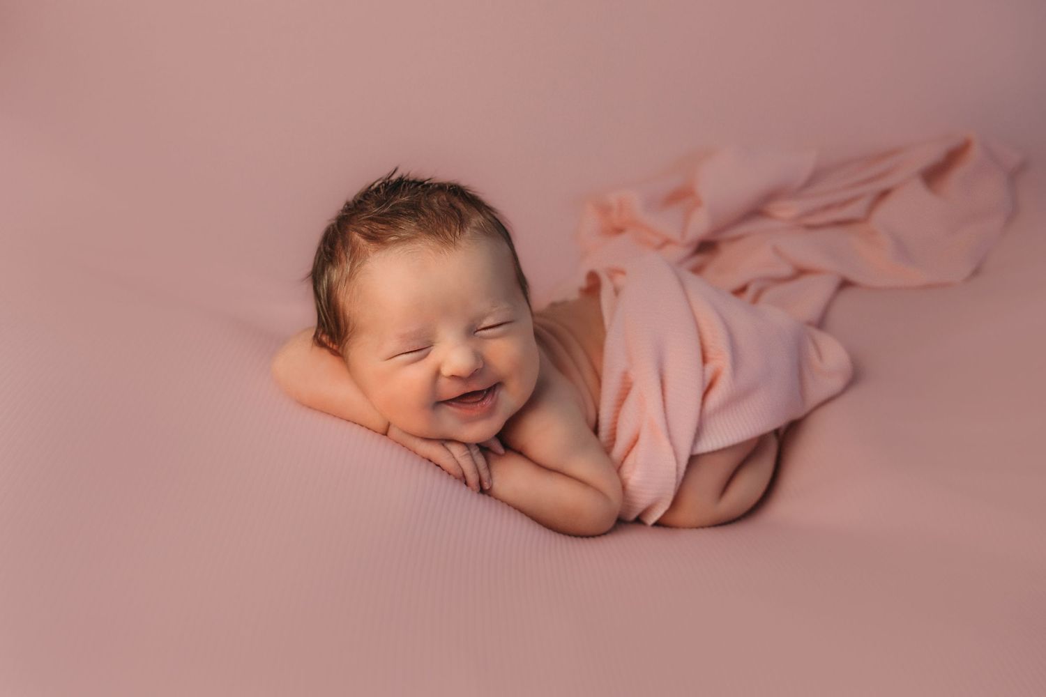 Adorable newborn baby photoshoot with soft pink tones and delicate wrapping.