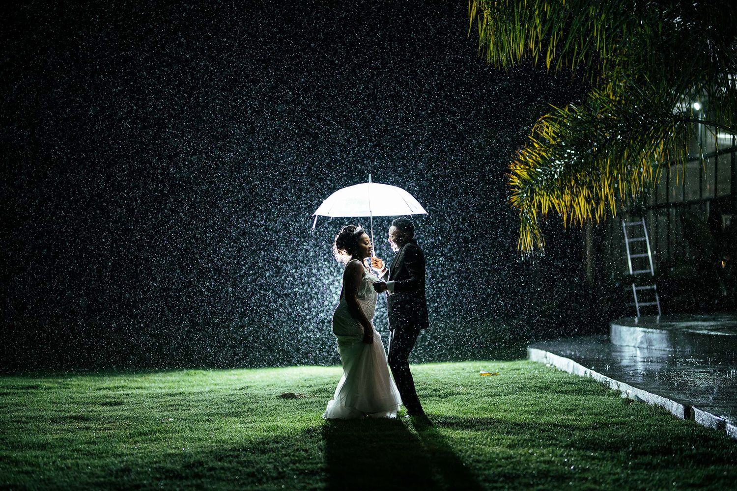 Silhouette of couple under illuminated umbrella in the rain at night.