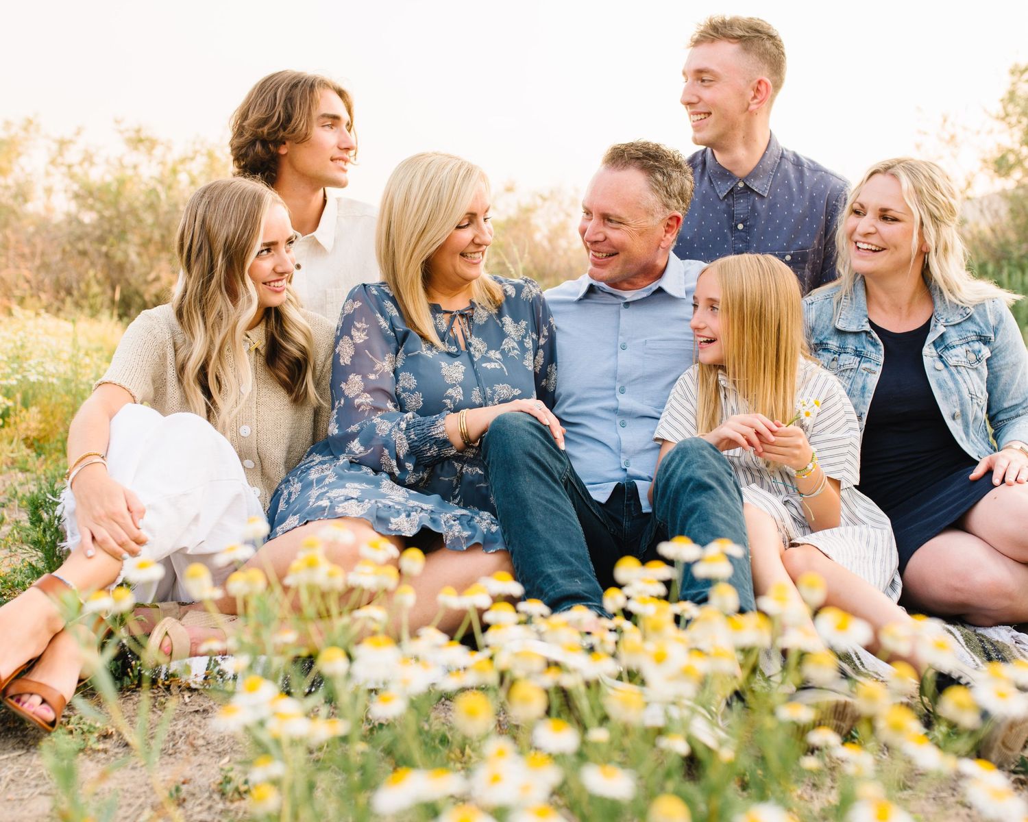 Extended family relaxes together on blankets among wildflowers in a sunny meadow.