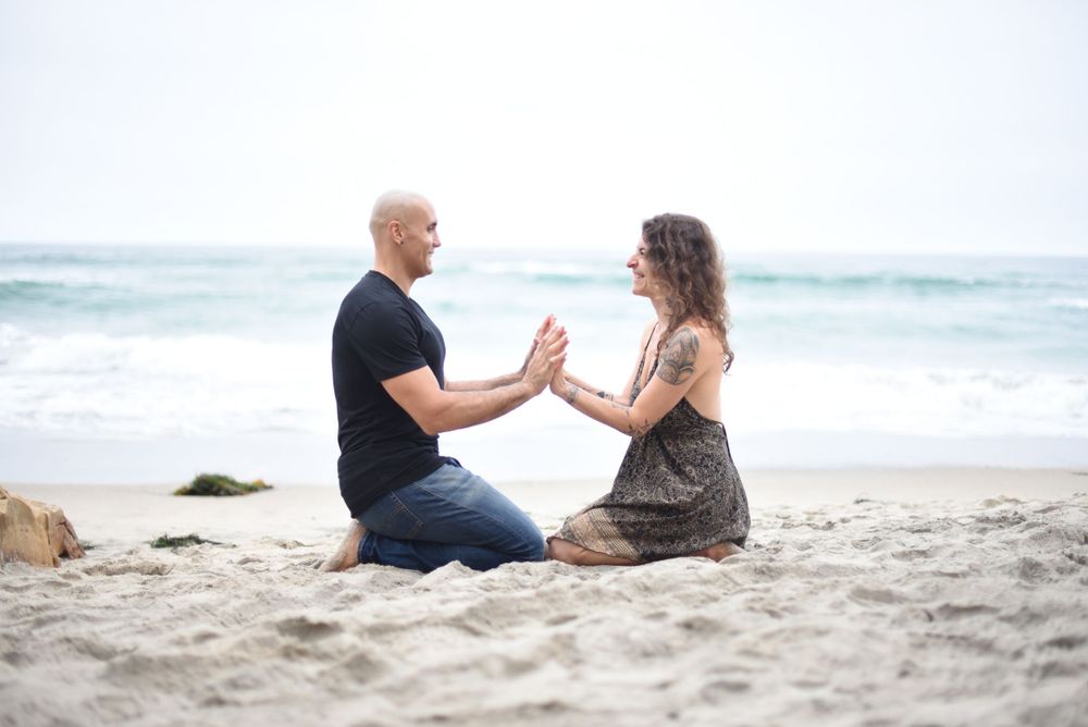 Two people sitting close together on sandy beach with ocean waves rolling in.