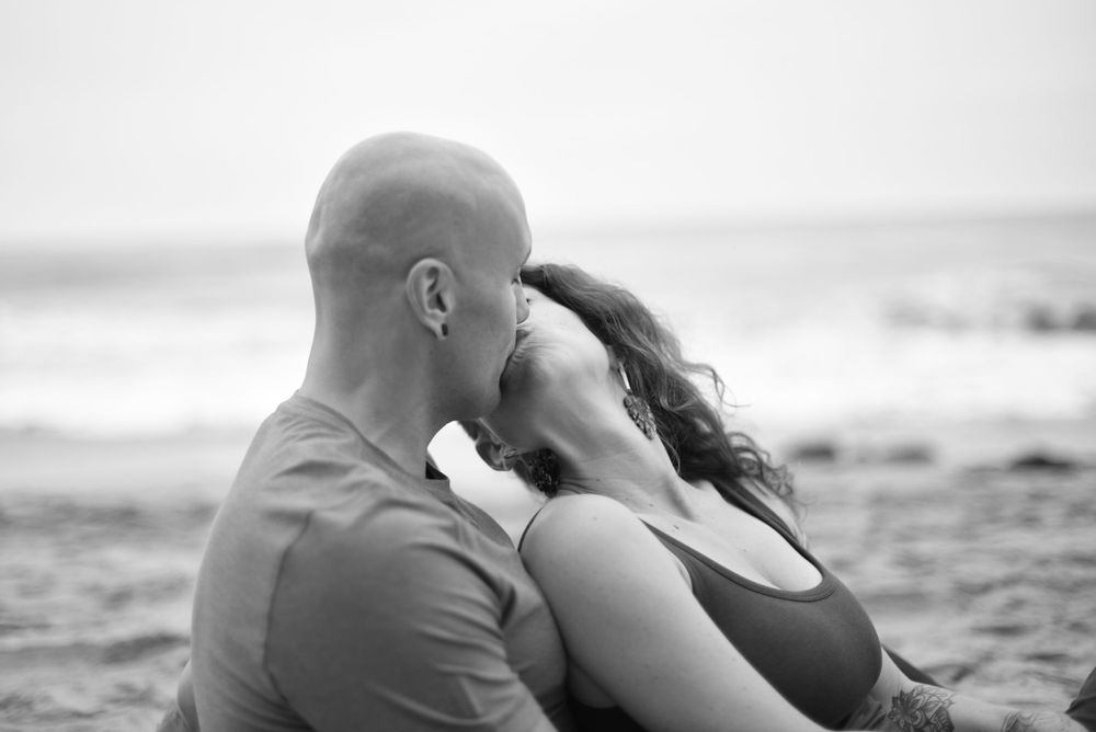 Couple cuddling together during sunset beach photoshoot.