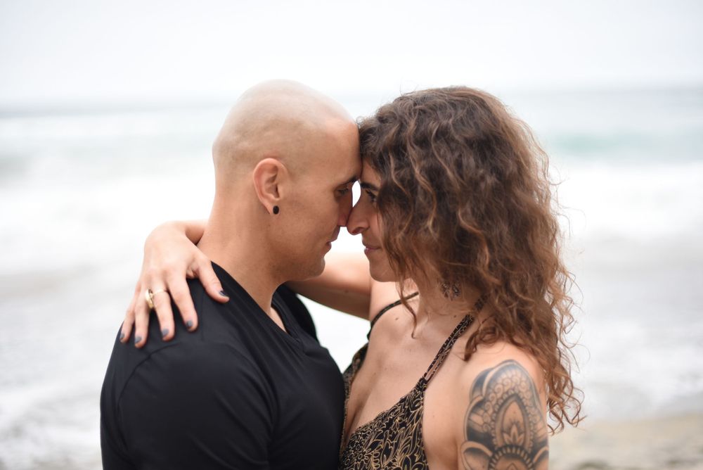 Intimate moment between couple cuddling on beach with ocean backdrop.