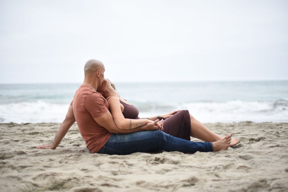 Two people share an intimate moment while lying on sandy beach.