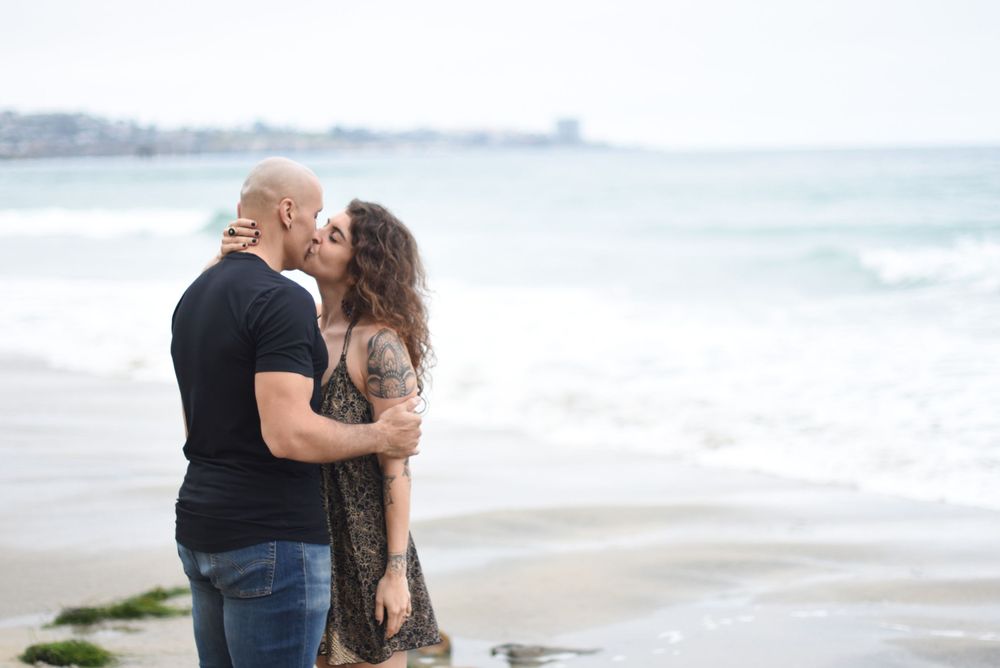 Couple embracing on sandy beach with ocean waves in background during sunset.