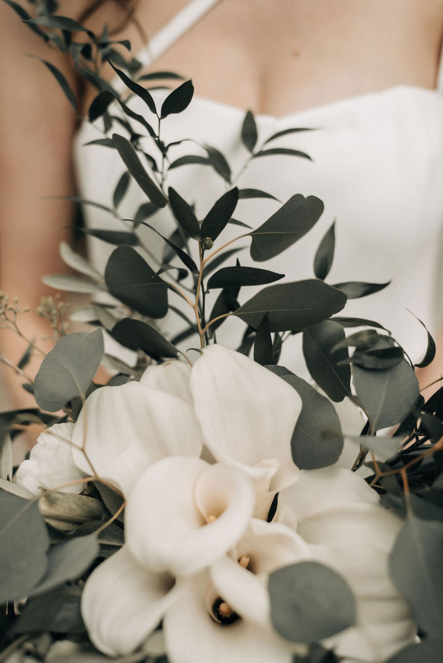 White calla lilies and eucalyptus leaves arranged in an elegant bridal bouquet.