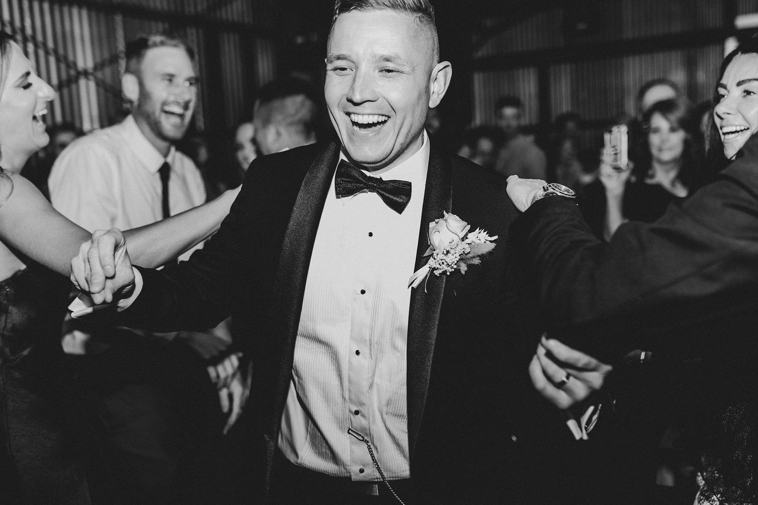 Joyful dancing and celebration at a black tie wedding reception in a rustic venue.