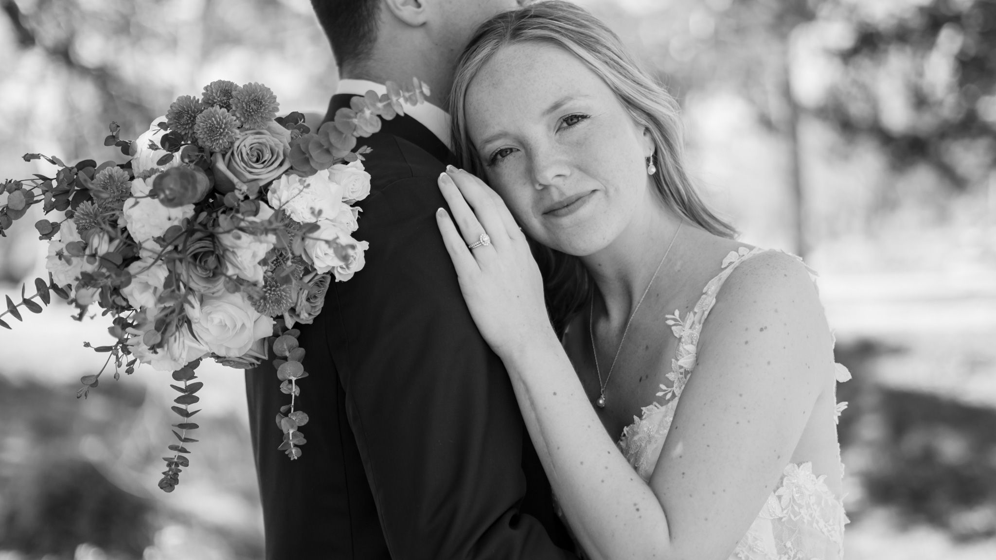 Intimate wedding moment with bride holding floral bouquet in black and white.