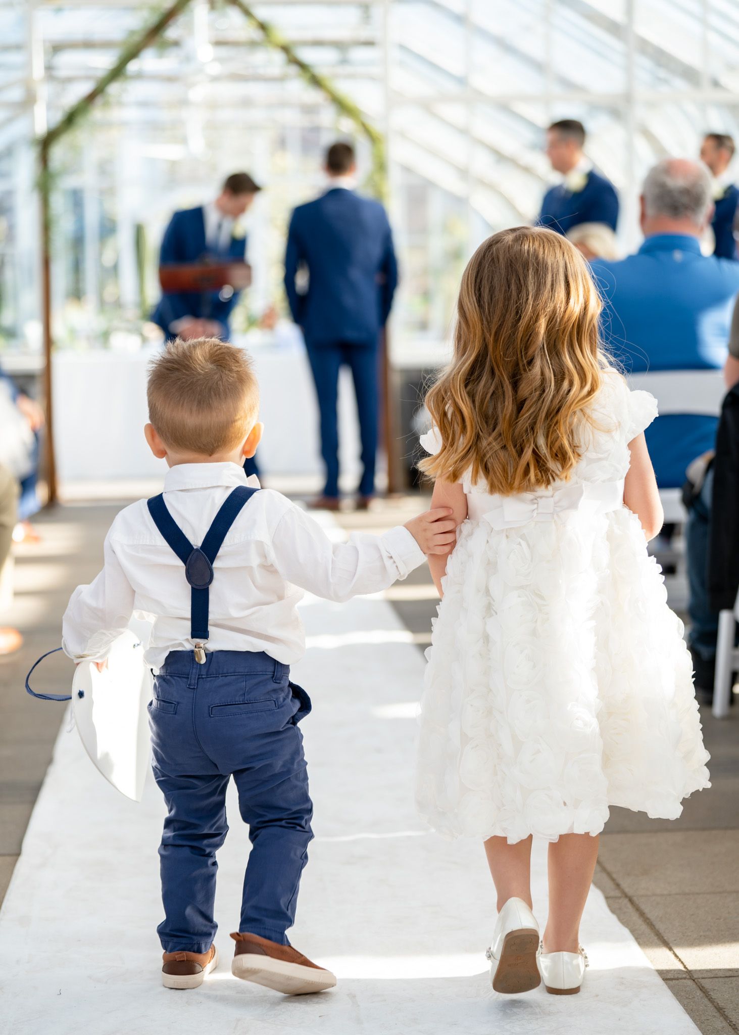 Children in white dresses and navy outfits walk together during wedding ceremony.