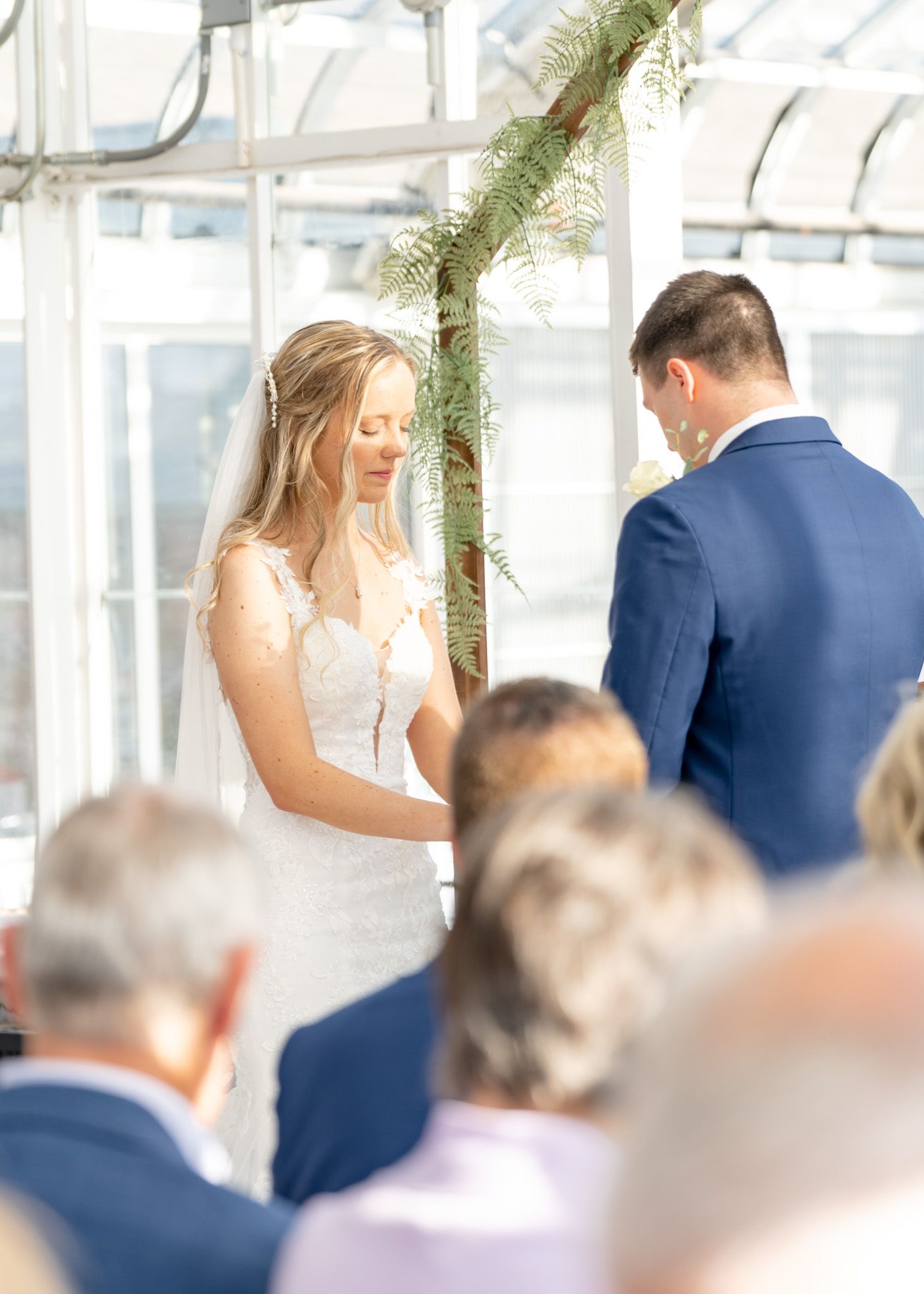 Wedding ceremony setup with white chairs and greenery decorations under a clear tent.