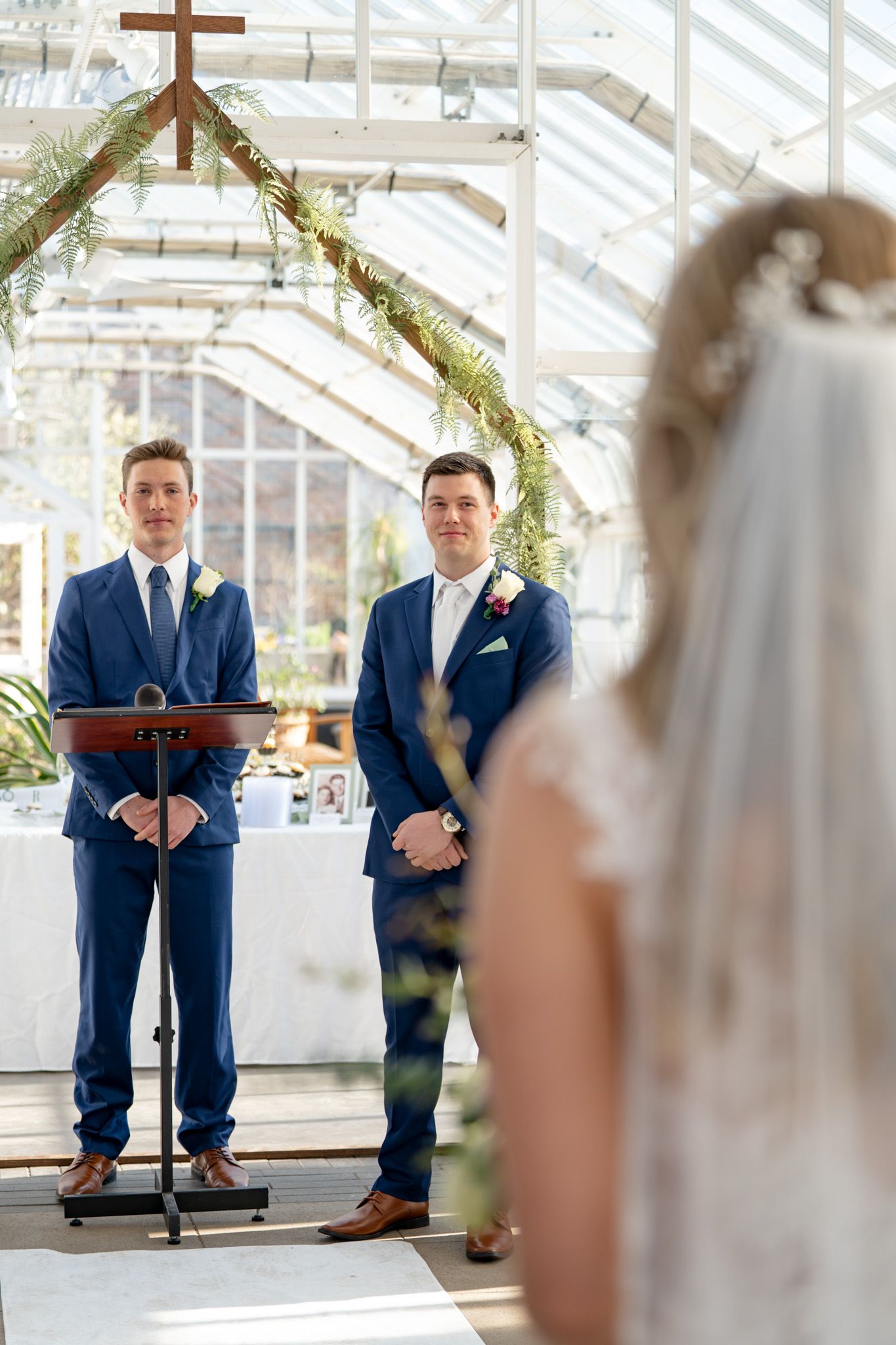 A wedding ceremony in a bright greenhouse with greenery and a wooden cross.