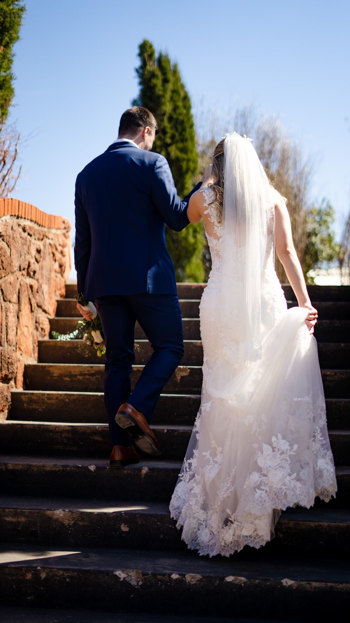 A bride and groom climbing stone steps together on their wedding day.