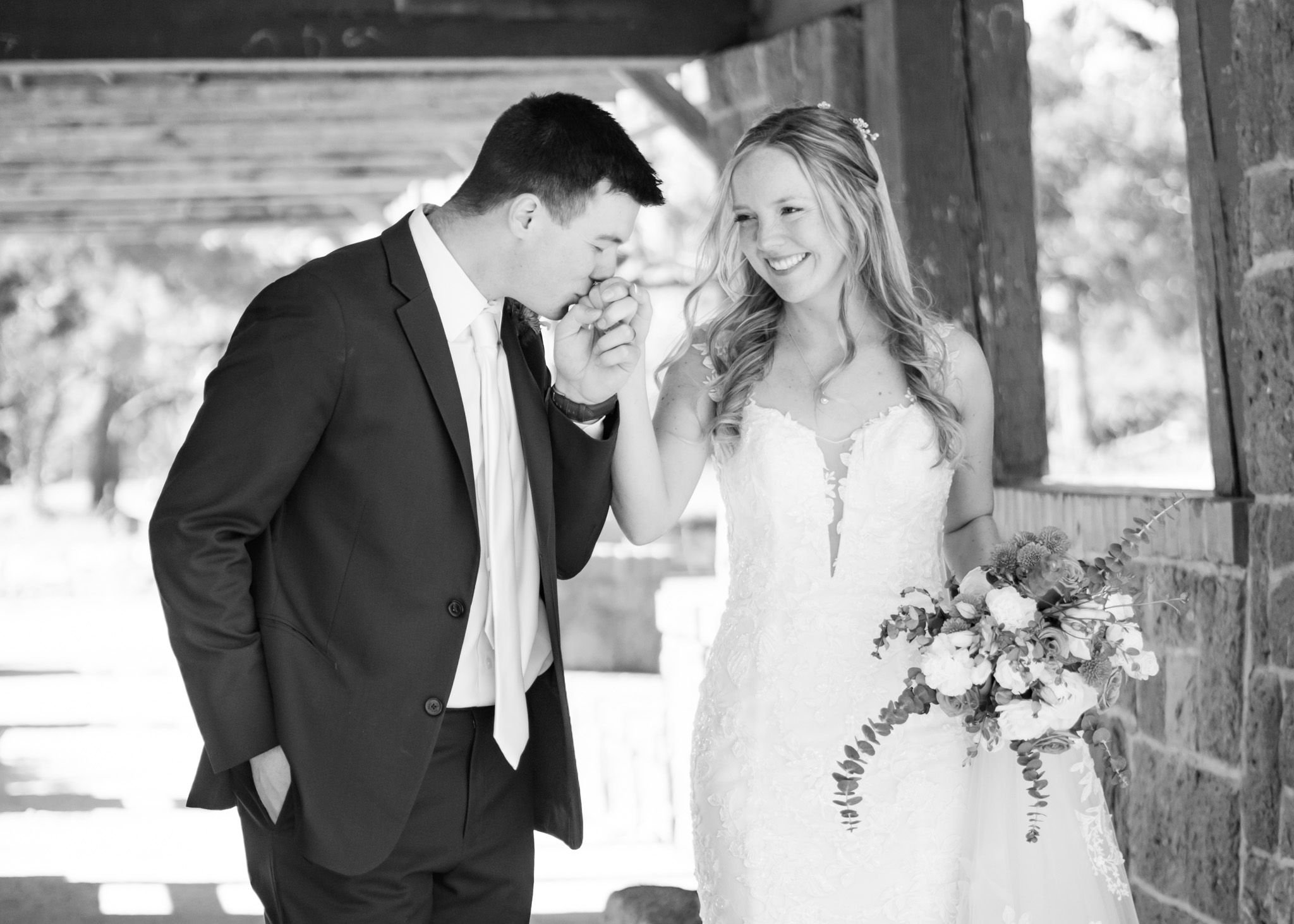 A black and white wedding photo showing a joyful moment between newlyweds under a covered area.