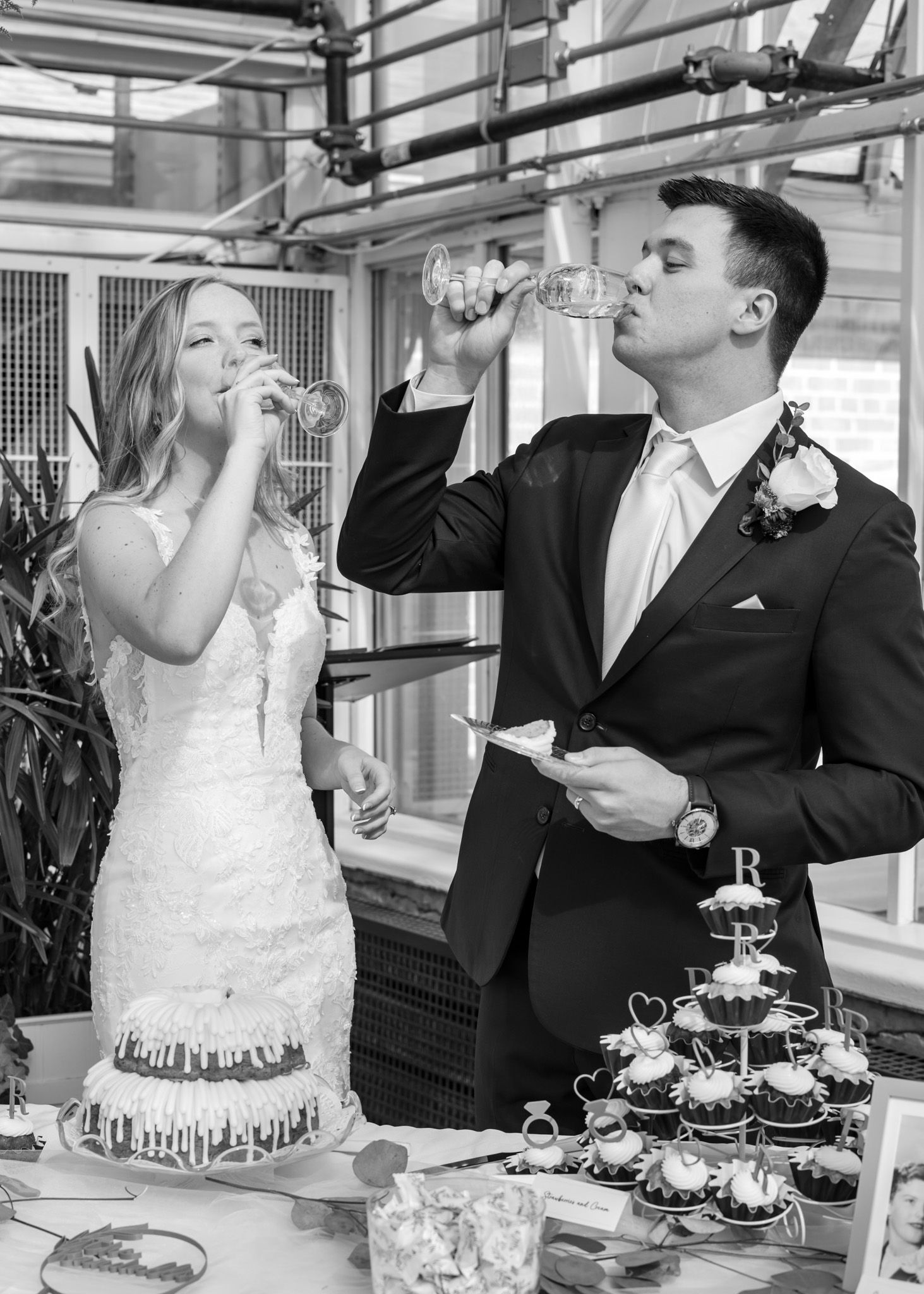 Newlyweds take a celebratory drink beside a tiered dessert display at their reception.