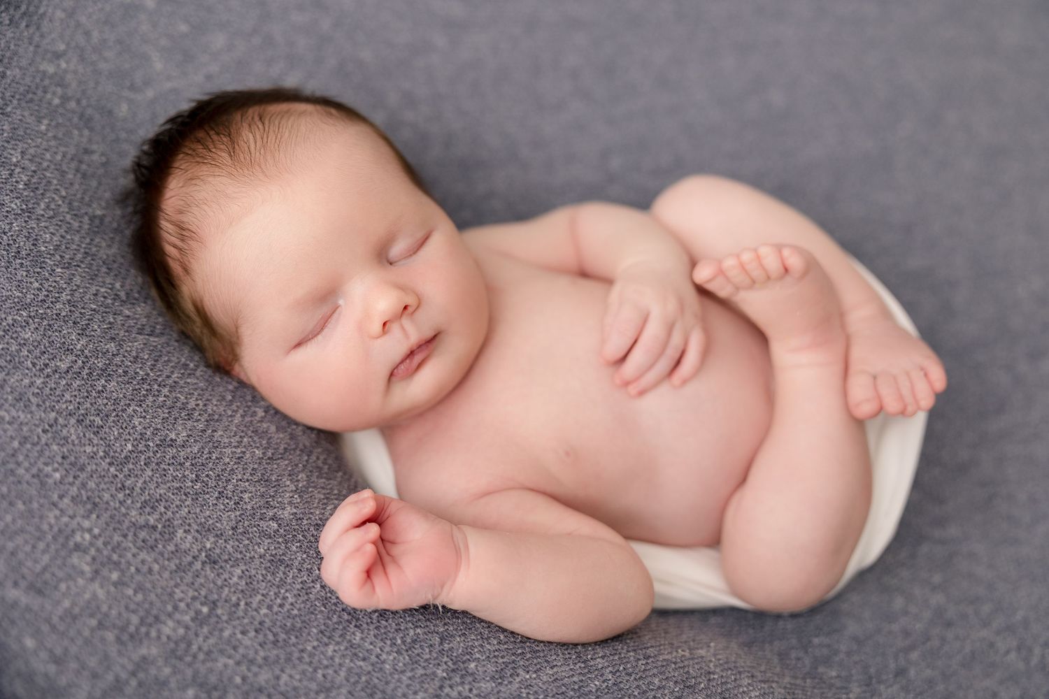Peaceful sleeping newborn baby lying on grey fabric during professional portrait session.