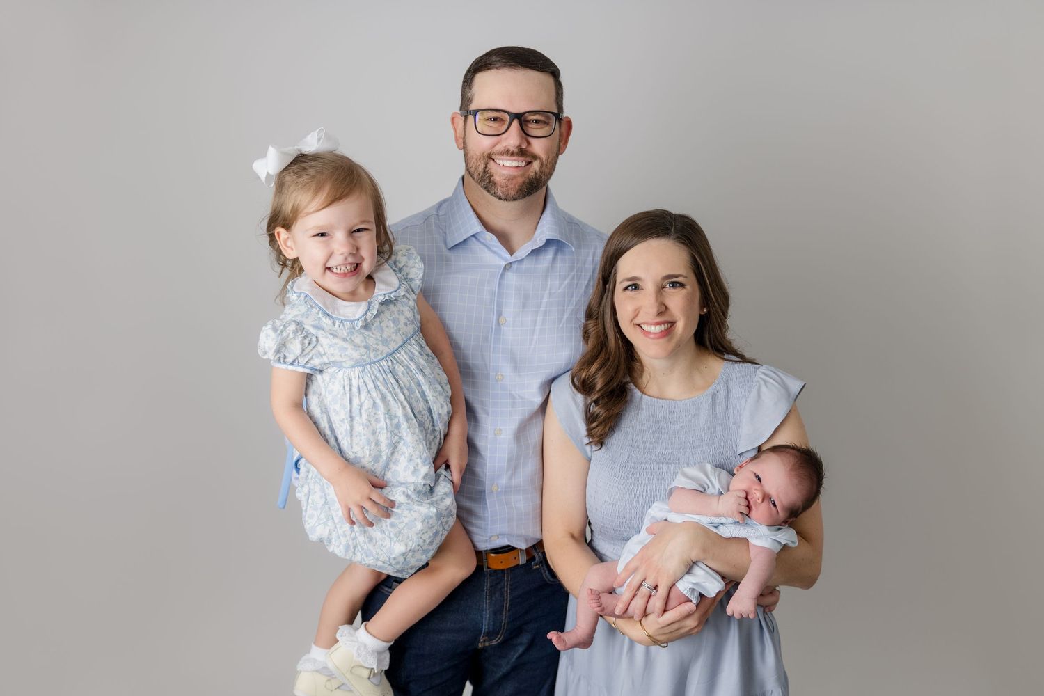 Studio family portrait with coordinating blue and grey outfits against neutral background.