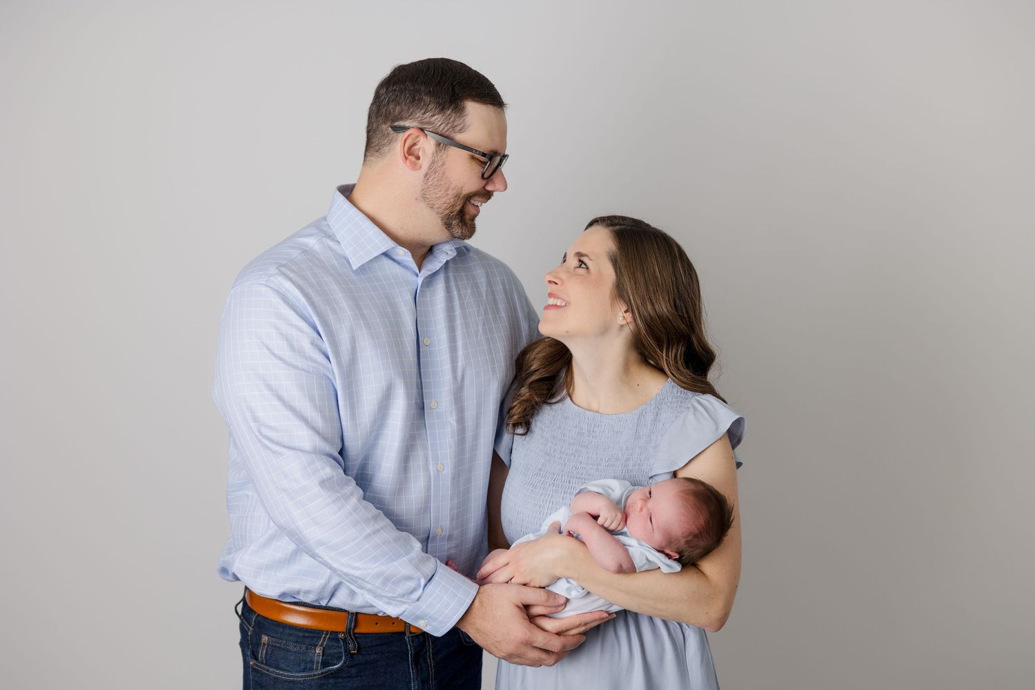 Intimate family moment captured against grey studio backdrop.