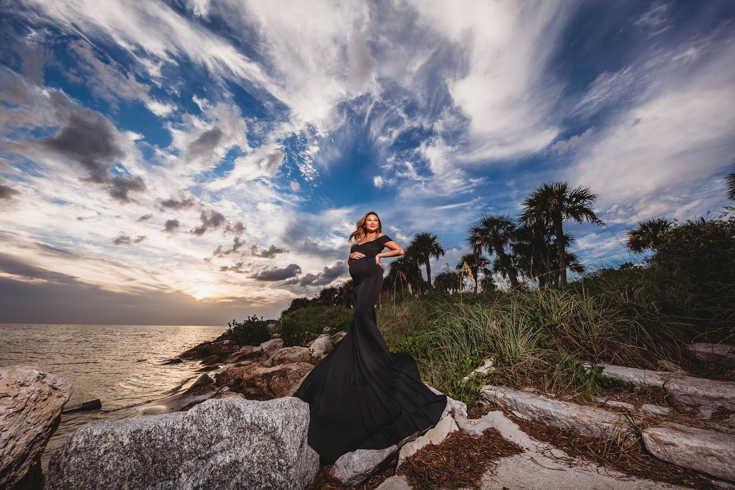 Dramatic sunset portrait on rocky coastal outcrop with dramatic cloudy sky.