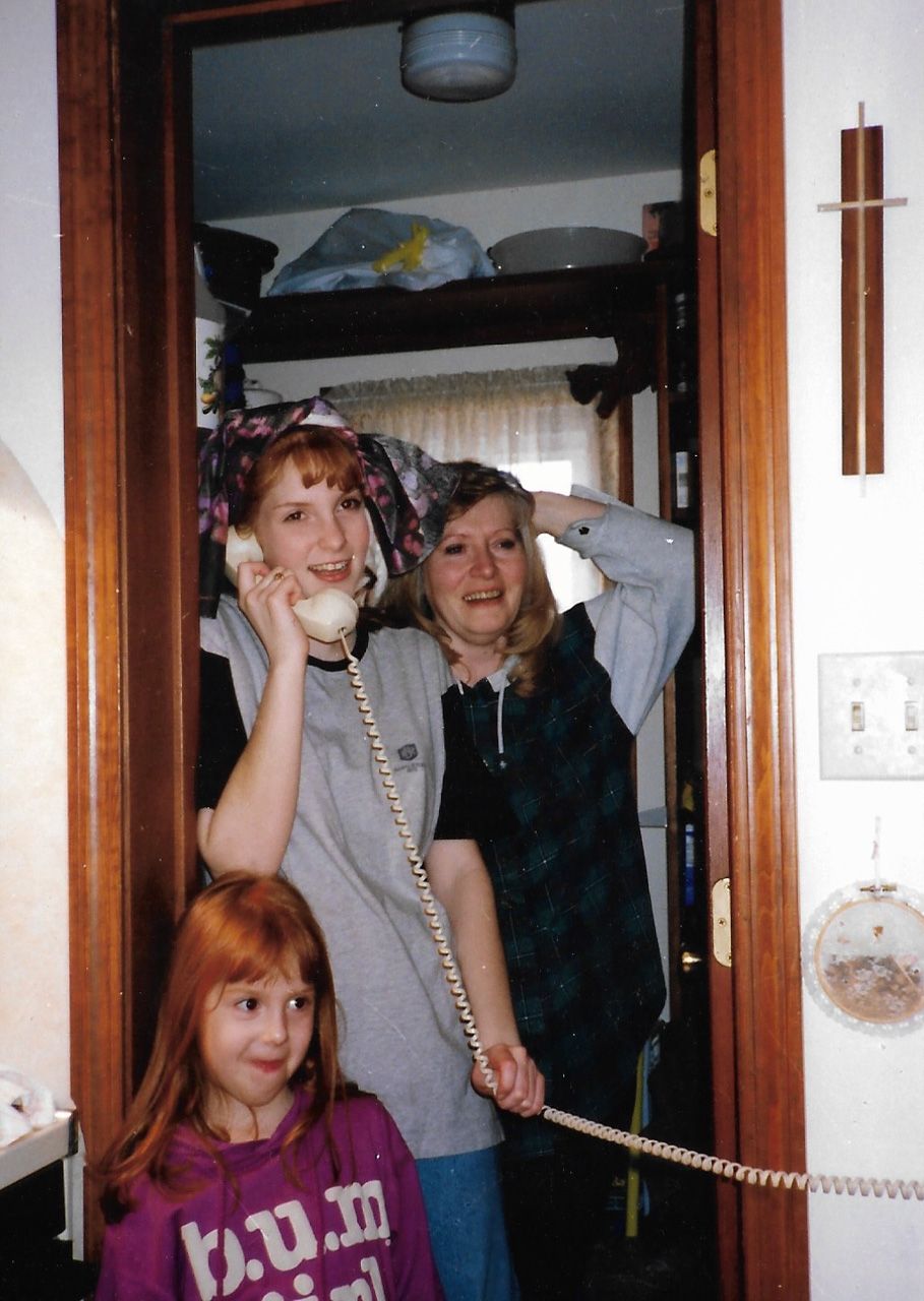 Three people posing in a doorway while talking on a corded telephone in a vintage photo.