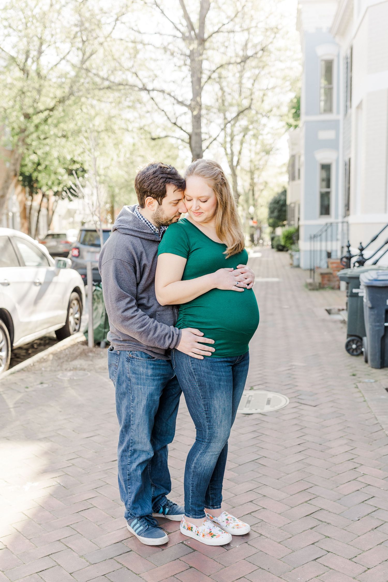 A couple embraces on a cobblestone street lined with spring trees.