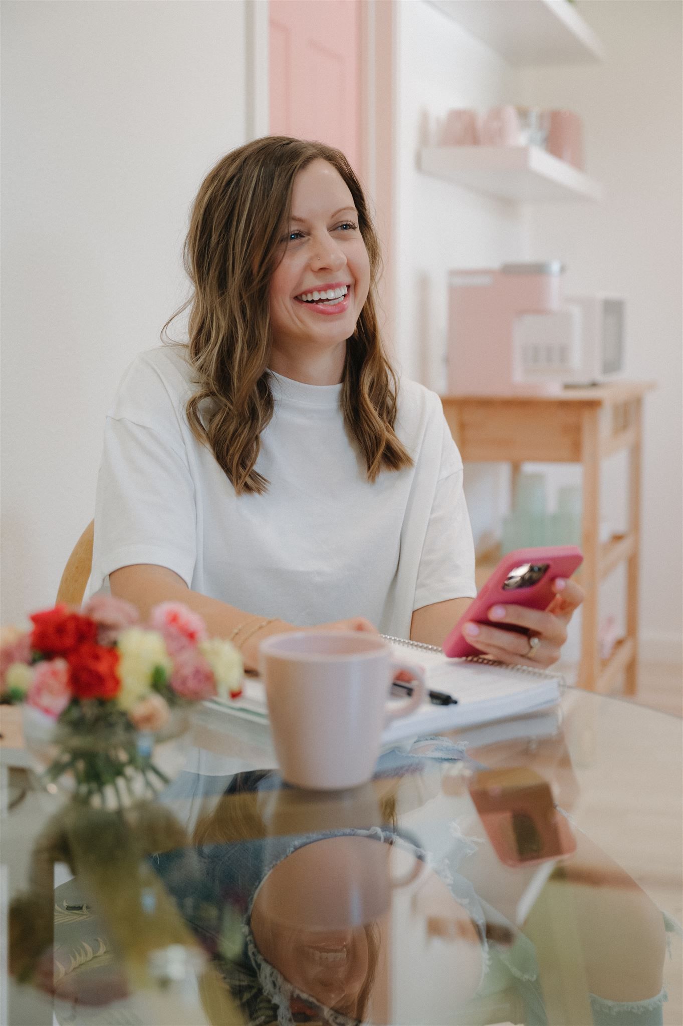Working at glass desk with pink mug and fresh flowers in bright modern space.