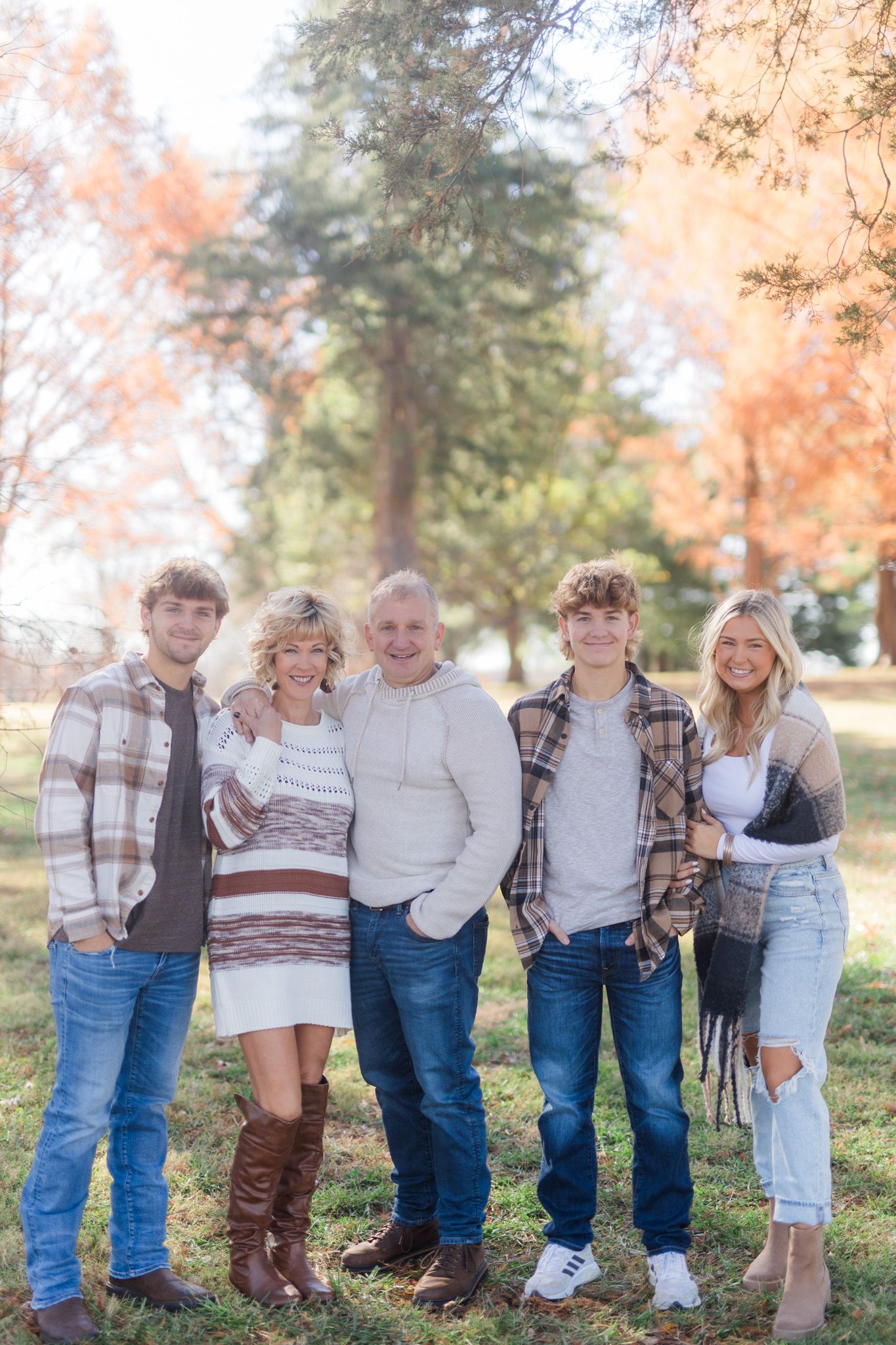 A family stands together outdoors in casual fall clothing against an autumn background with trees.