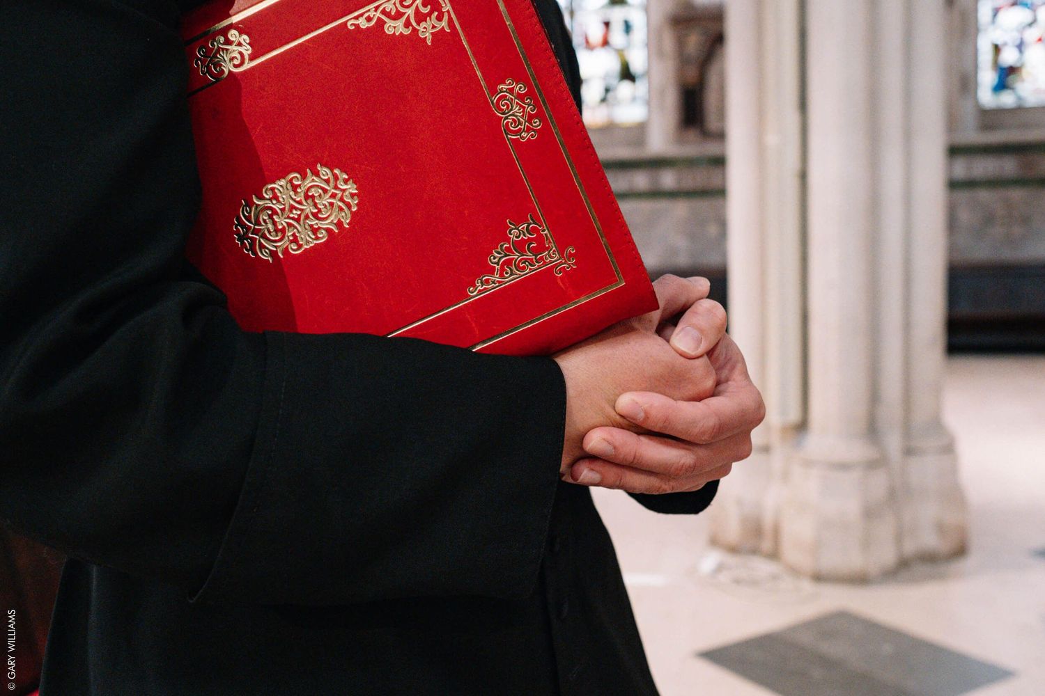 Hands holding a red ceremonial book with gold embossed details in a church setting.
