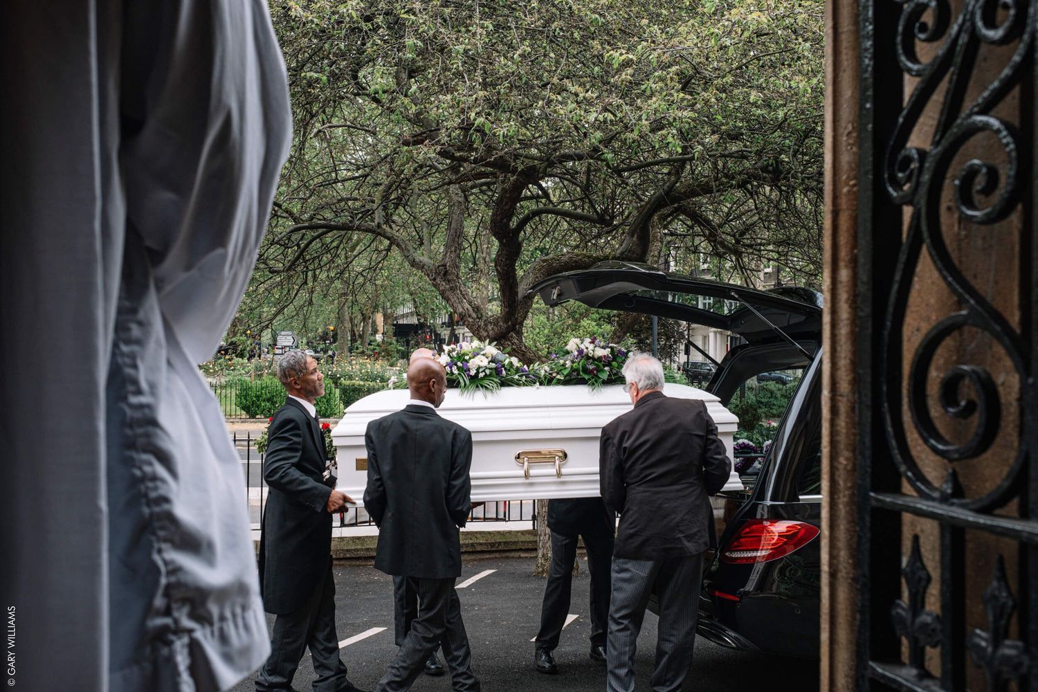 Pallbearers carrying a white casket outside a church during a funeral service.