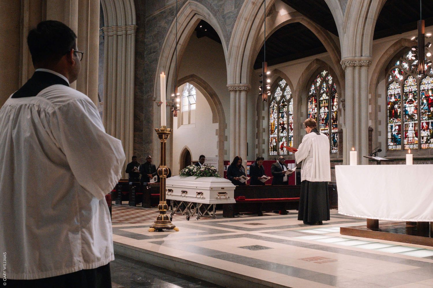 Interior of a church during a service showing Gothic arches and stained glass windows.
