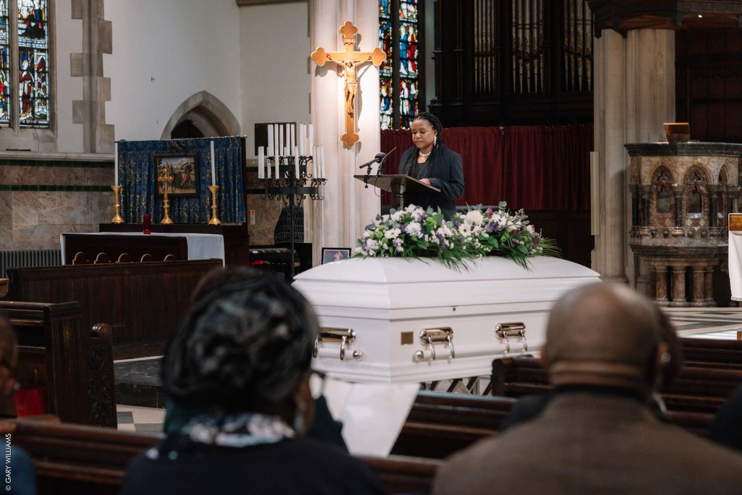 A white casket with floral arrangements during a church funeral service.